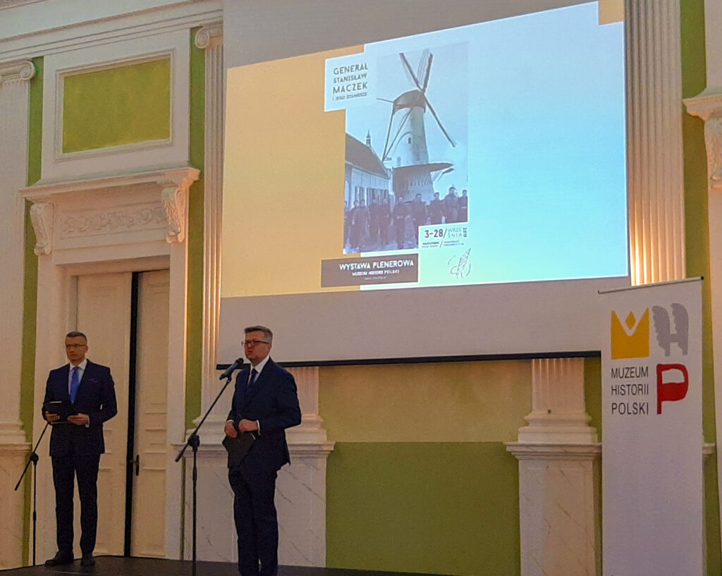 Przemówienie przy ekranie z plakatem wystawy o generale Maczku