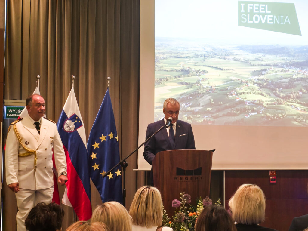 Wystąpienie przy mównicy obok flag Słowenii i Unii Europejskiej