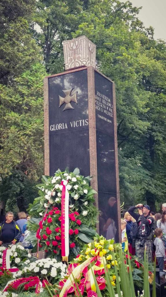 Pomnik Gloria Victis z wieńcami i biało-czerwonymi kwiatami