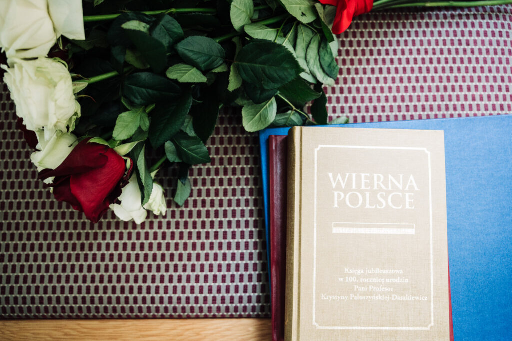 Księga jubileuszowa Wierna Polsce obok białych i czerwonych róż