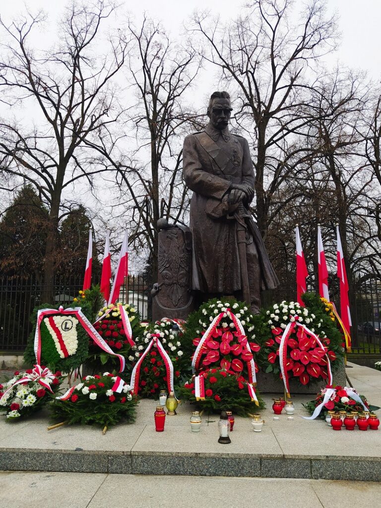 Pomnik Józefa Piłsudskiego, biało-czerwone flagi, wieńce i znicze
