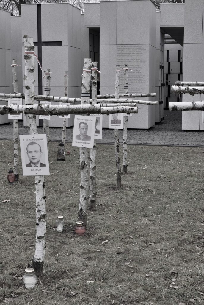 Brzozowe krzyże z portretami upamiętnionych przed pomnikiem Niezłomni Wyklęci