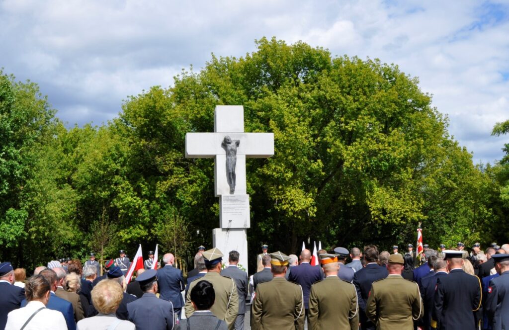 Uczestnicy uroczystości i wojskowa asysta przed pomnikiem z krzyżem